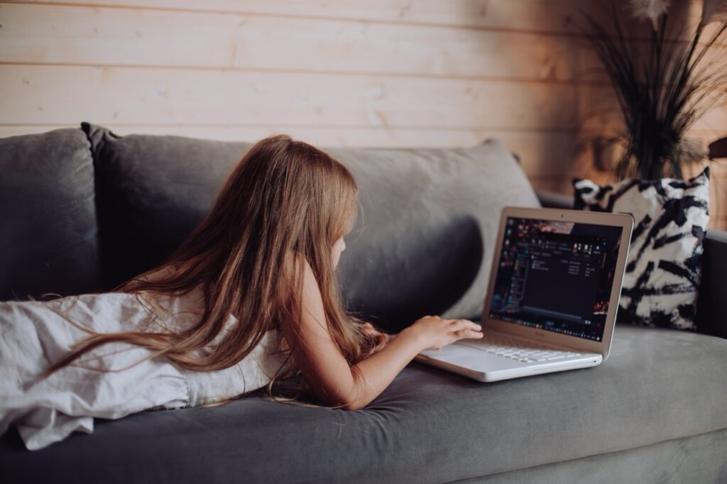 Young girl lying on a sofa using a laptop at home in the evening.